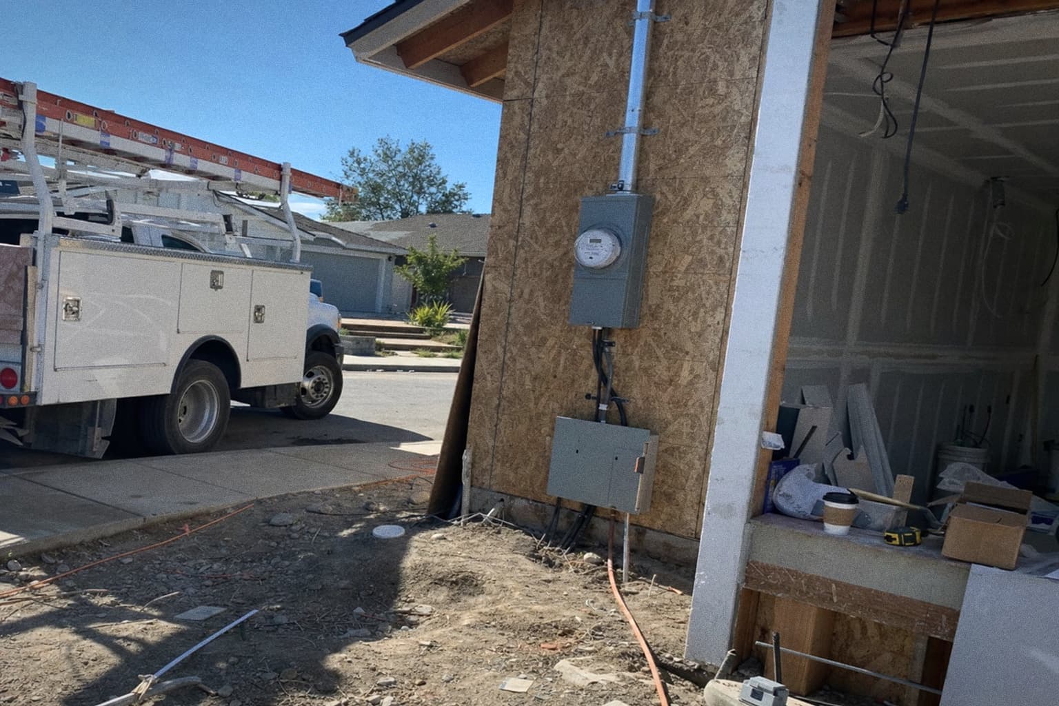 A new service mast, meter socket and panel on a half-finished house, with a contractor truck at the kerb.